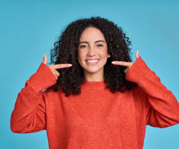 "Smiling Latina woman pointing at white teeth, promoting dental whitening care
